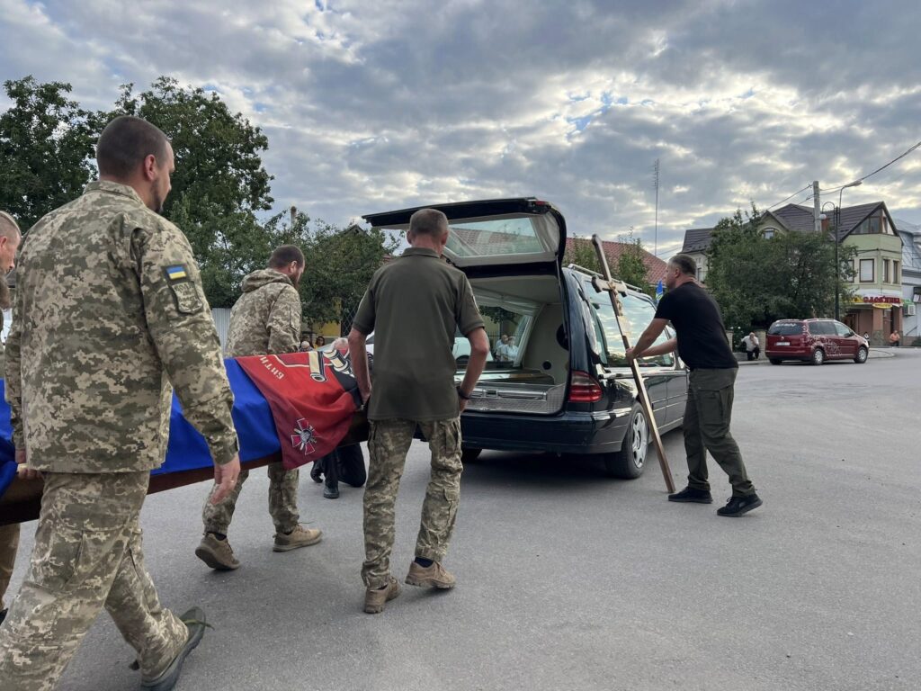 Військові поміщають труну у катафалк на вулиці