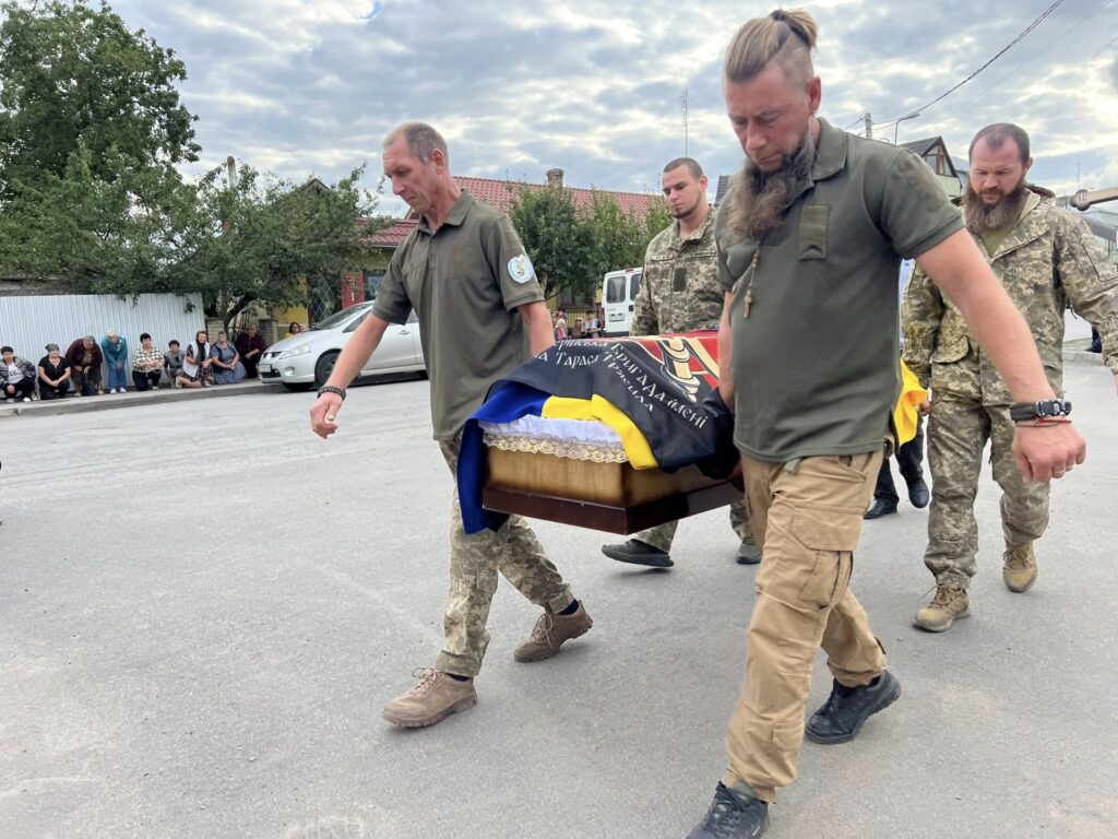 Військові несуть труну вулицею, люди спостерігають.