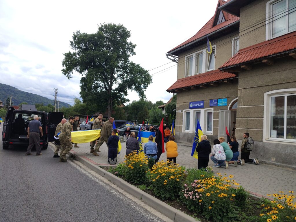 Люди з прапорами на тротуарі біля будівлі поліції.