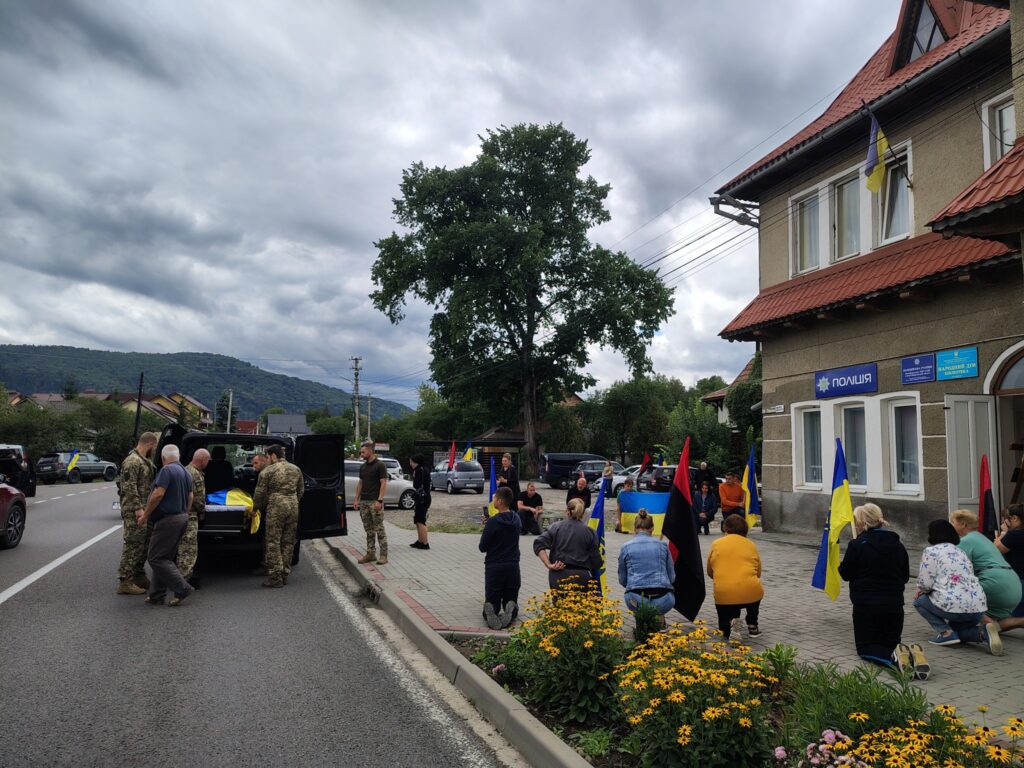 Люди віддають шану, українські прапори, вулиця, поліція.