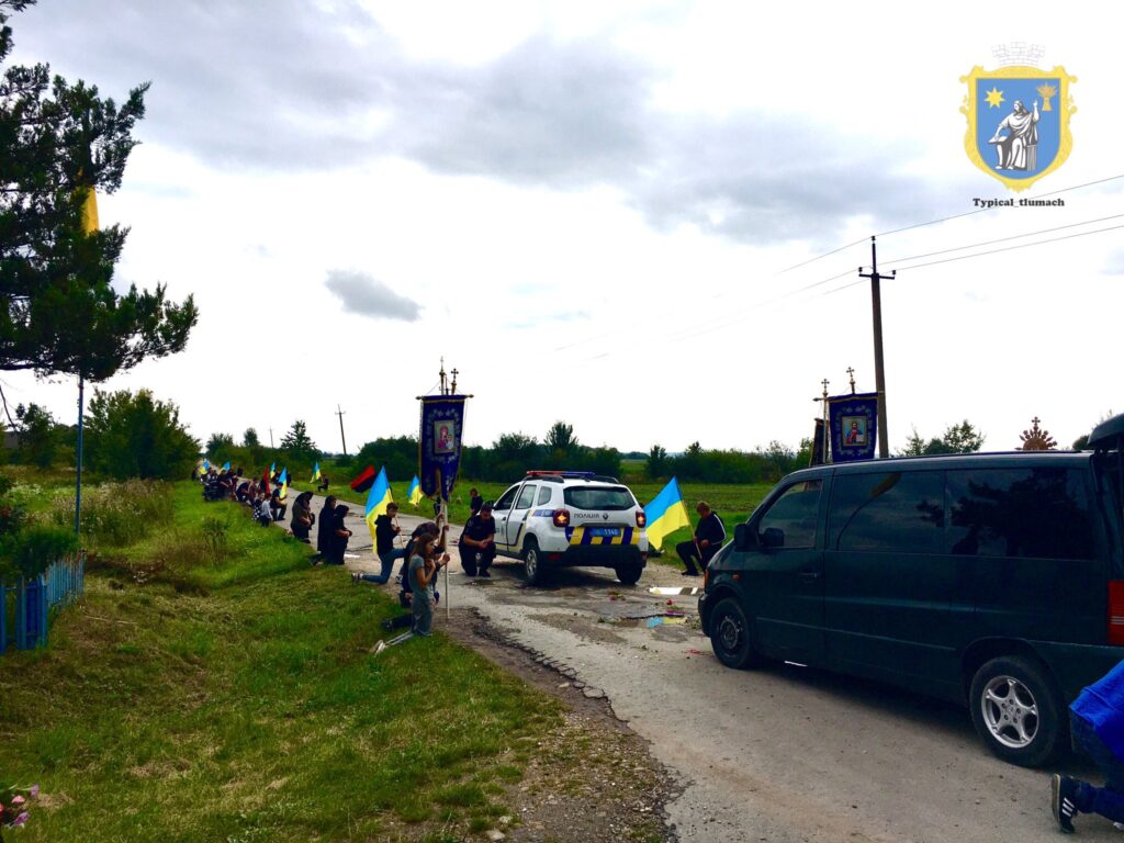 Люди з прапорами на дорозі, автомобілі та транспаранти.