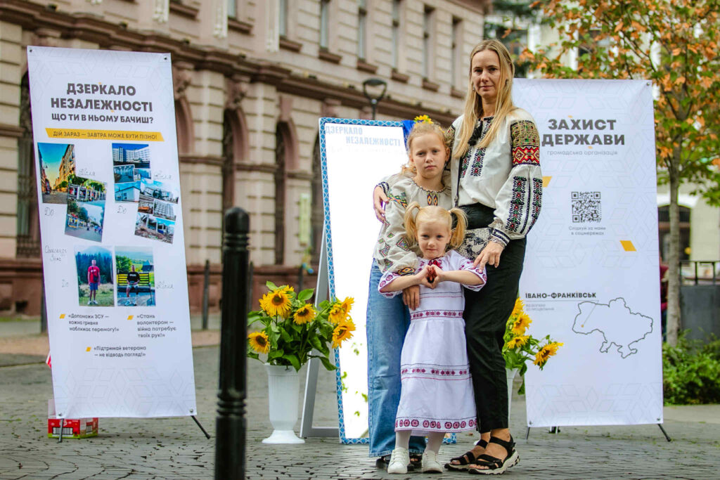 Жінка з дітьми у традиційному одязі біля банера.