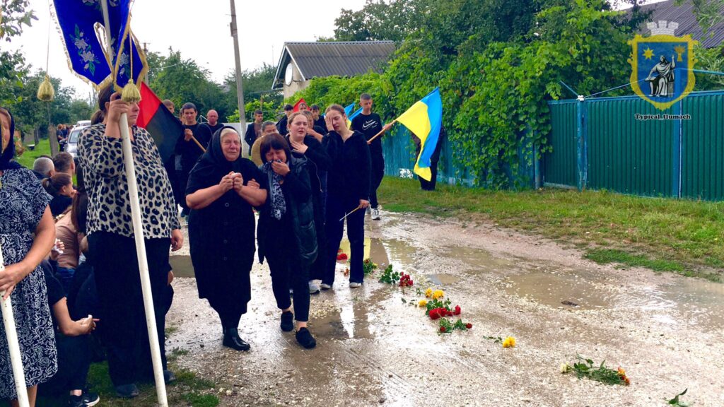 Люди на похоронній процесії з українськими прапорами.