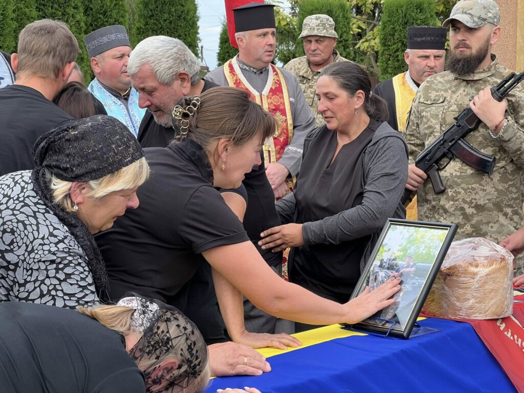 Люди в скорботі біля фотографії війни