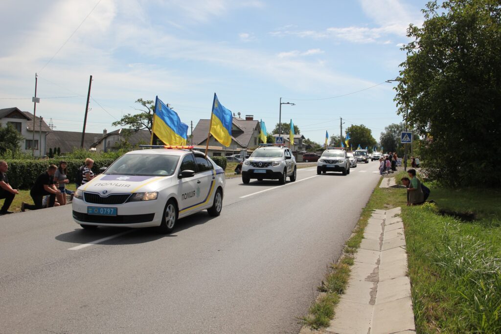 Поліційні машини з українськими прапорами на дорозі.