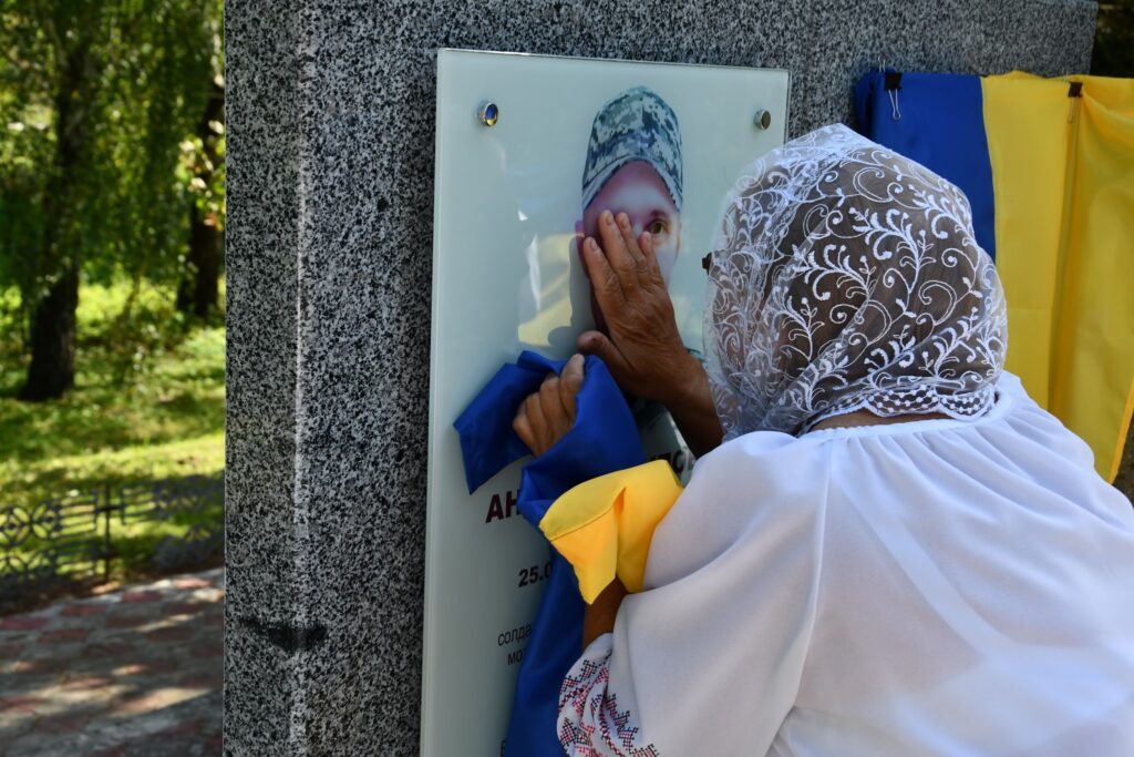 Жінка торкається меморіалу з прапором України.
