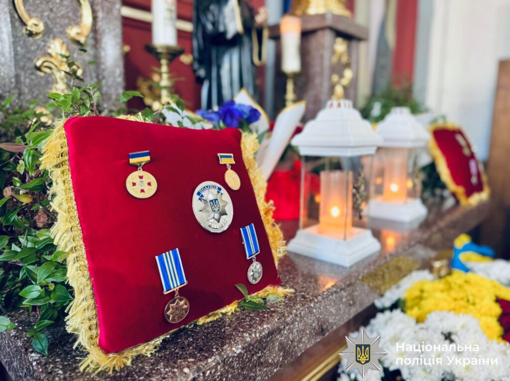 Нагороди на червоній подушці, свічки навколо.