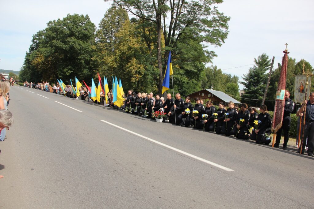 Люди з прапорами на колінах біля дороги