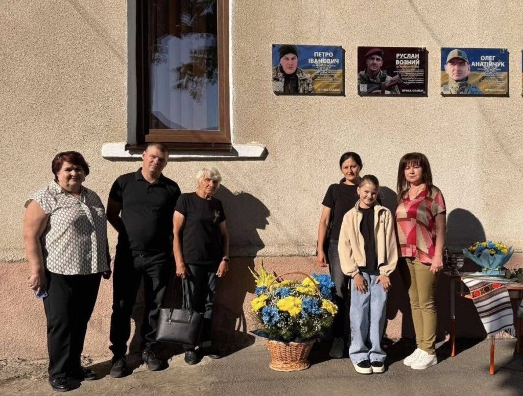 Люди стоять біля будівлі з портретами героїв.