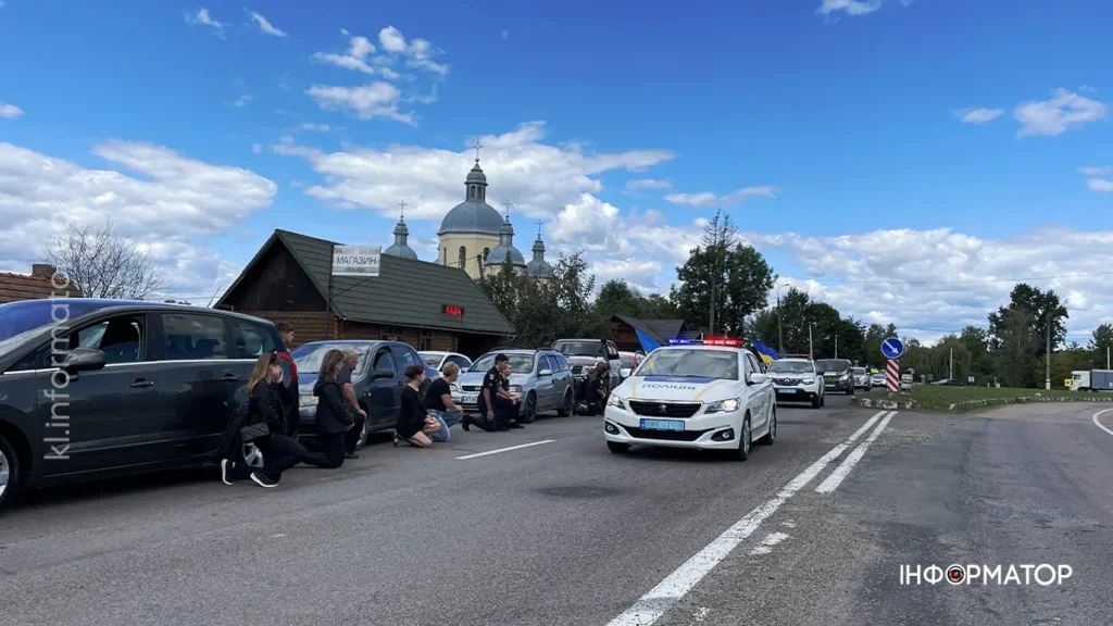 Люди на колінах, автомобілі, церква, крізь дорогу проїжджає поліція.