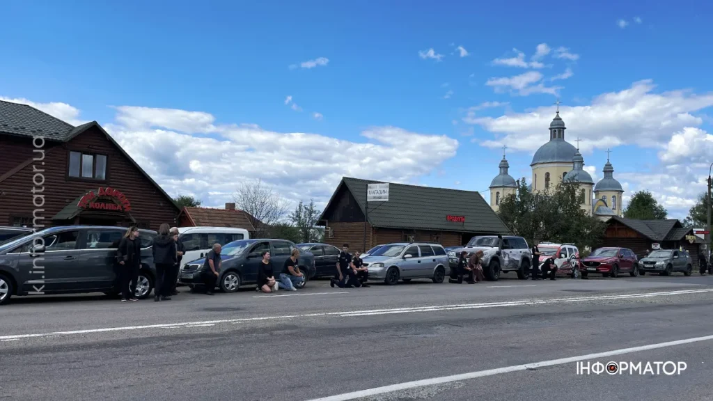 Люди поруч із машинами біля дороги і церкви.
