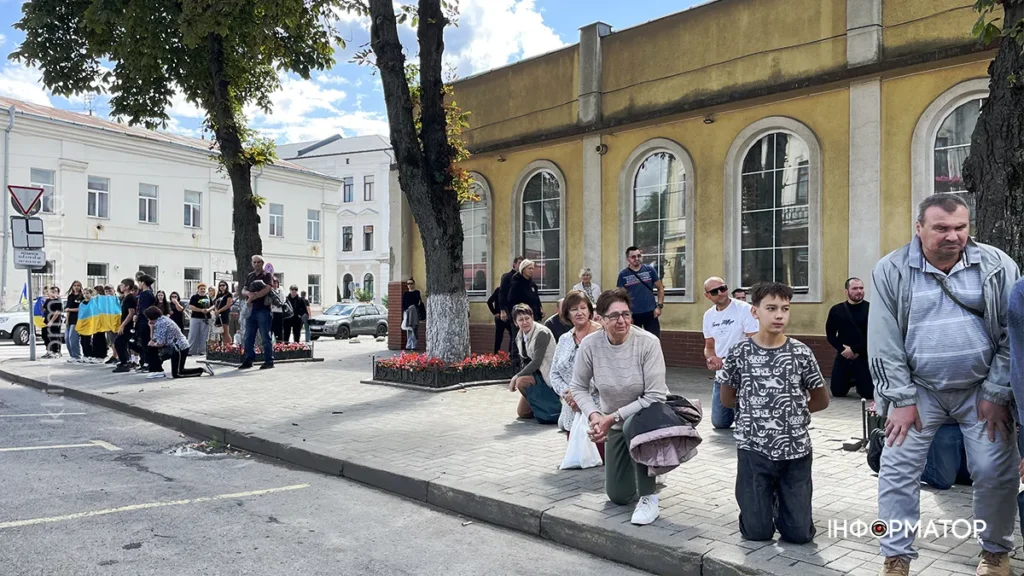 Люди на вулиці з прапором України на фоні.
