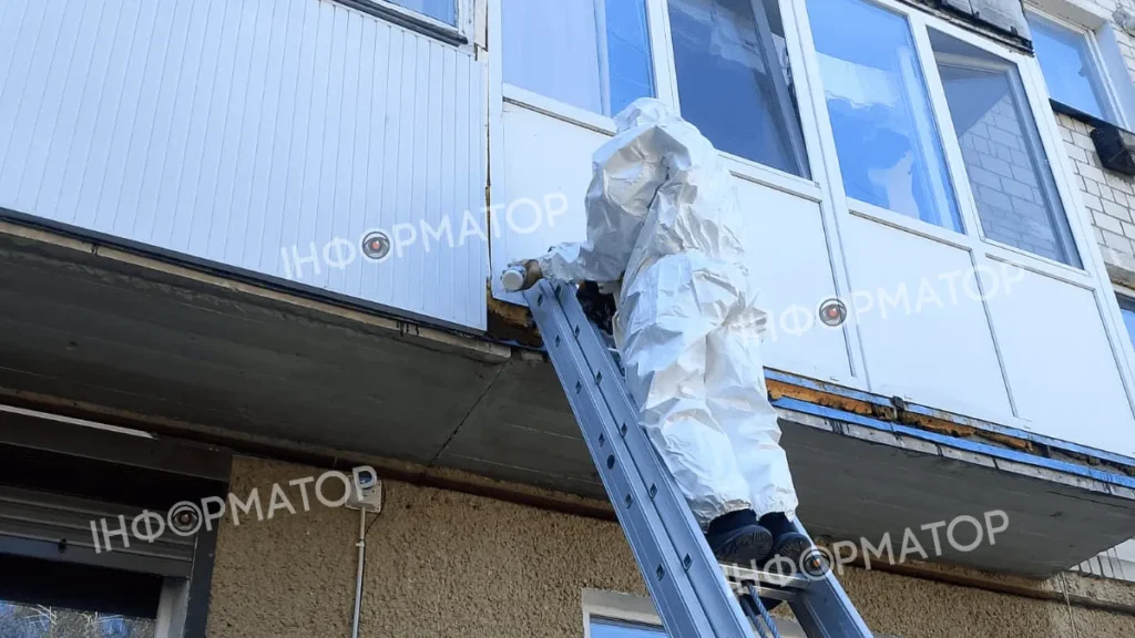 Чоловік в захисному костюмі на драбині біля будинку