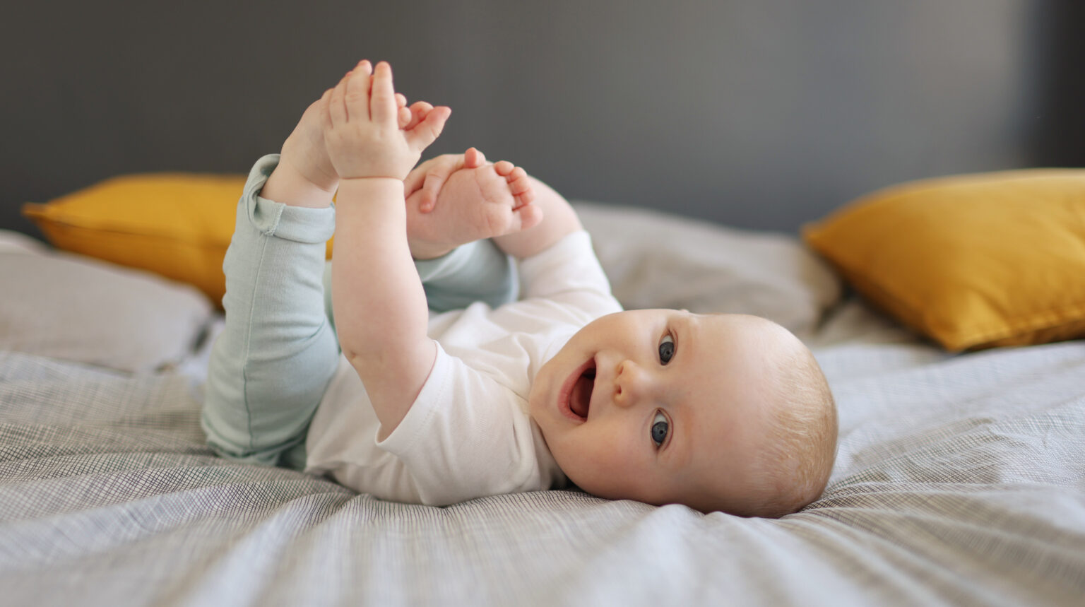Малюк грається на ліжку, тримаючи ноги