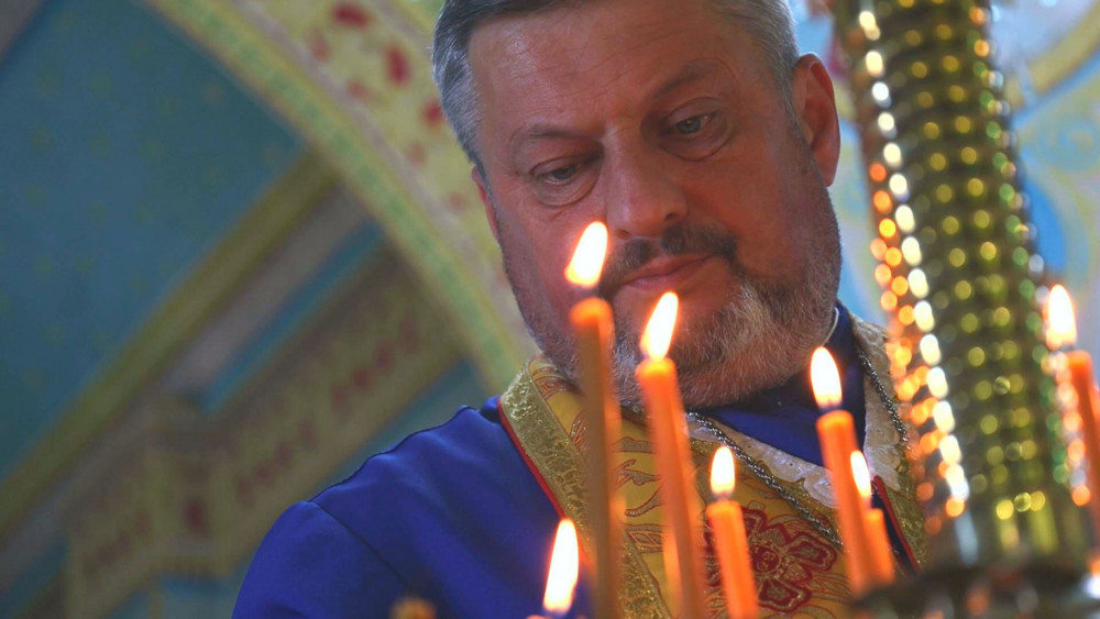 Священик запалює свічки в церкві