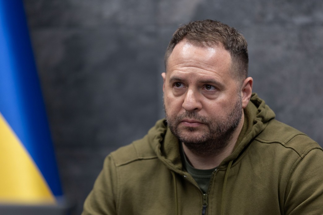 Чоловік у зеленій куртці на фоні прапора
