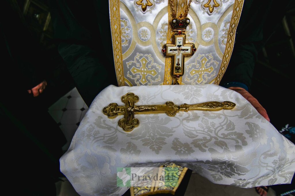 Священник тримає золоте розп'яття на вишитій тканині.