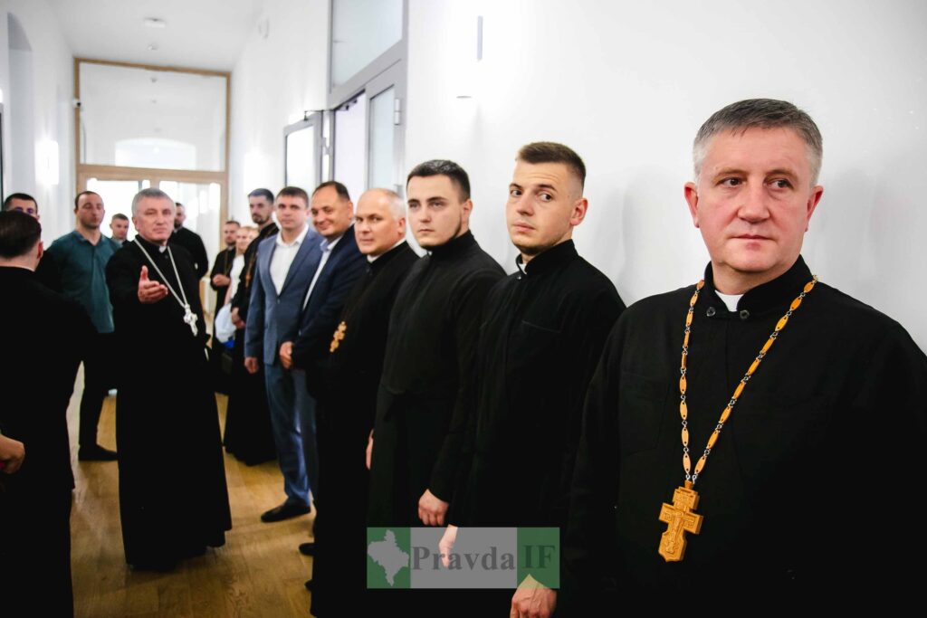 Священики у коридорі, чоловіки в костюмах поруч.