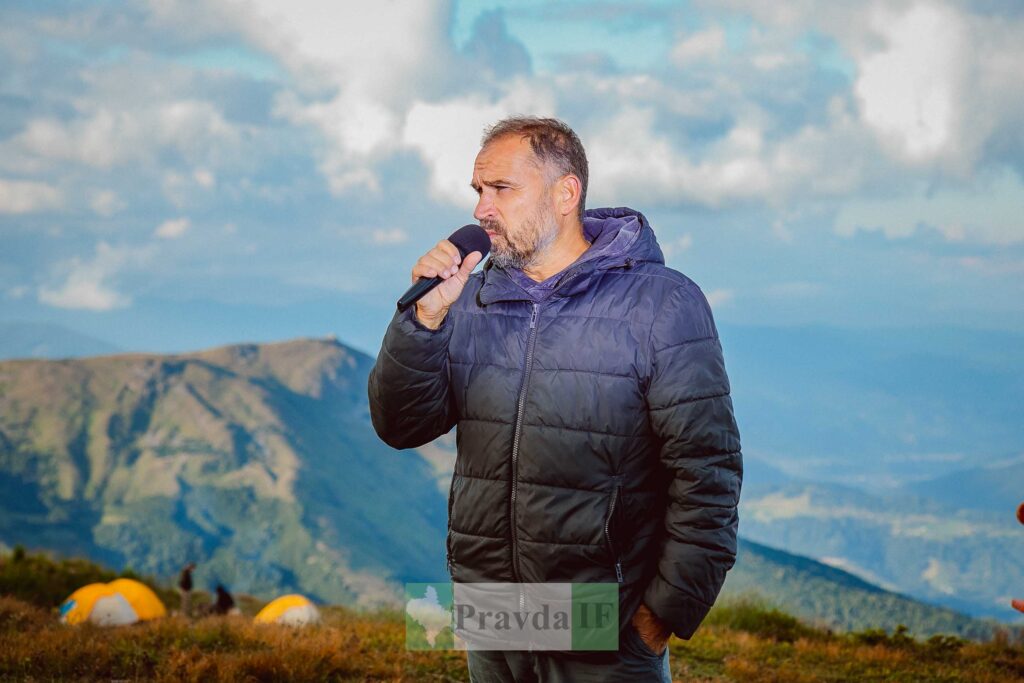 Чоловік з мікрофоном на тлі гірського пейзажу.