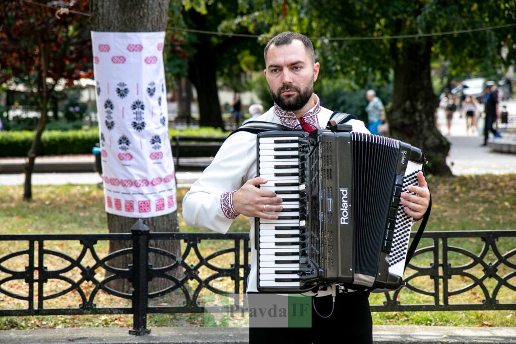 Чоловік у вишиванці грає на акордеоні у парку.