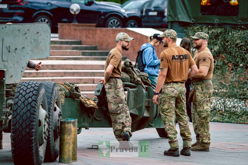 Солдати в камуфляжі розмовляють біля військової техніки.