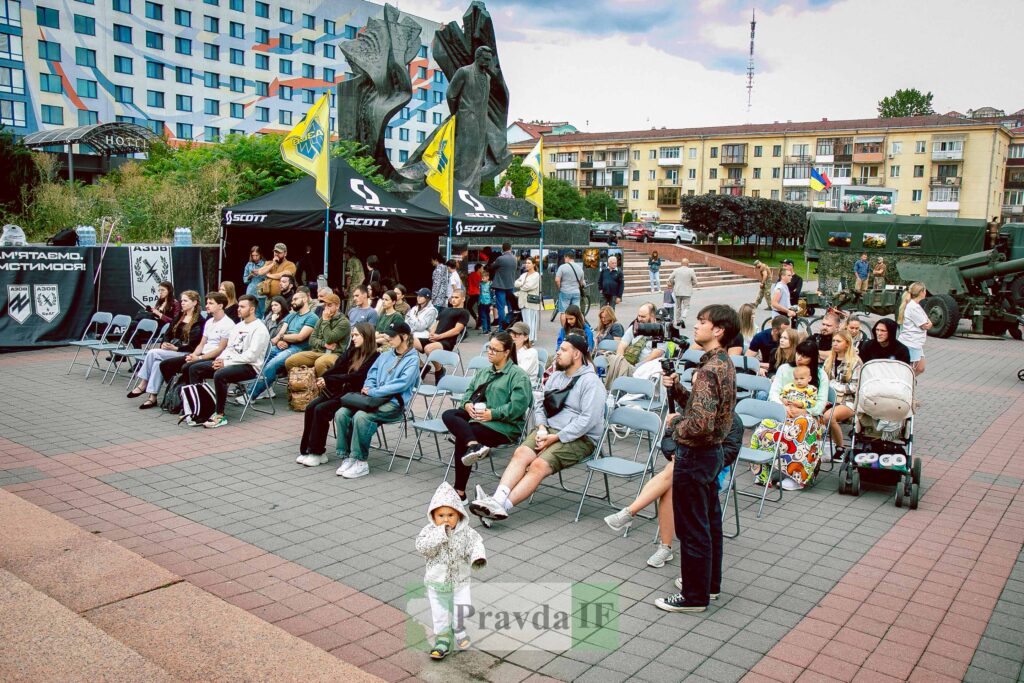 Люди сидять на вулиці перед кіосками з прапорами.