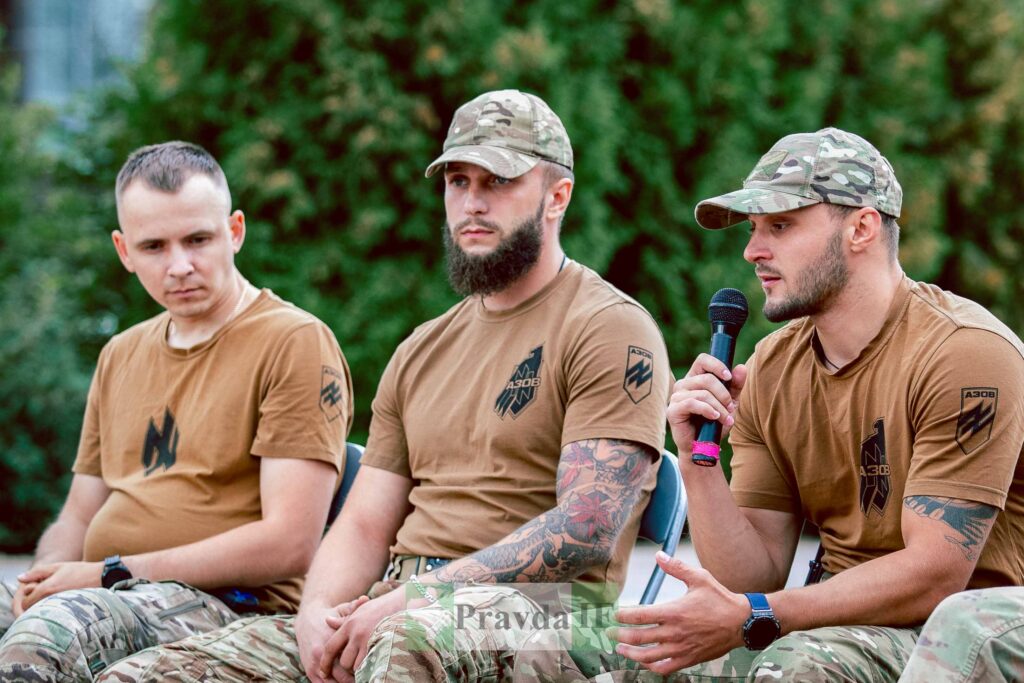 Три військових у формі з мікрофоном, зелений фон.