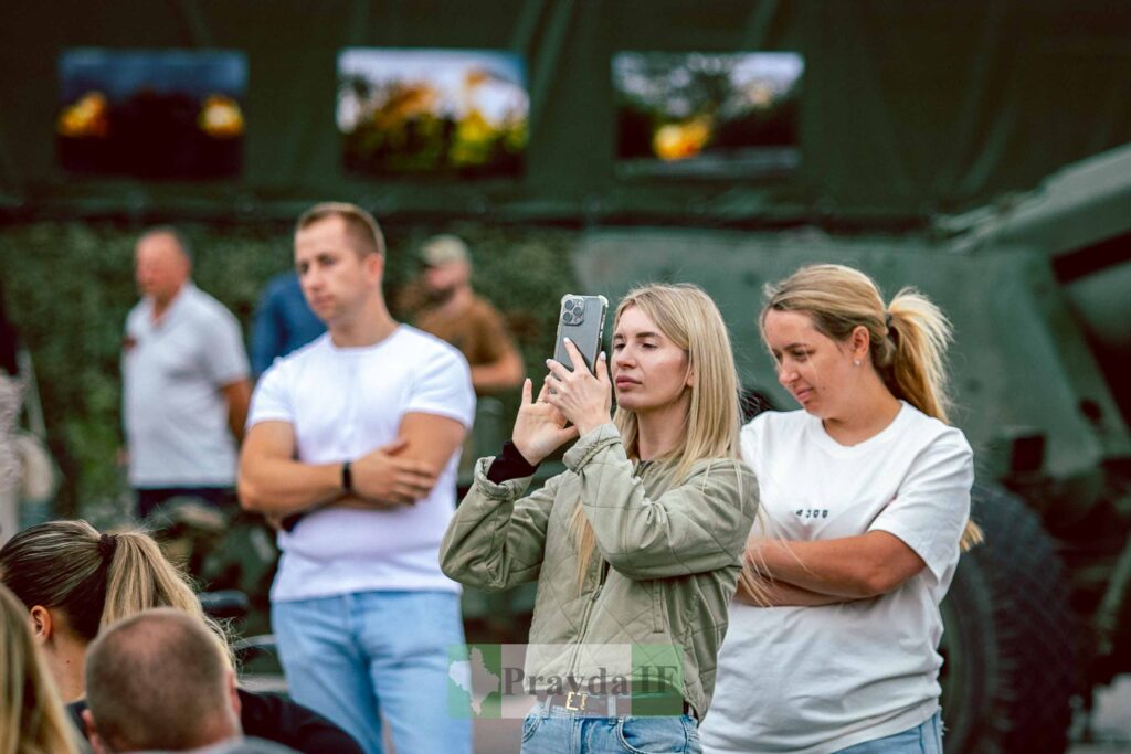 Жінка фотографує на відкритому повітрі, натовп позаду.