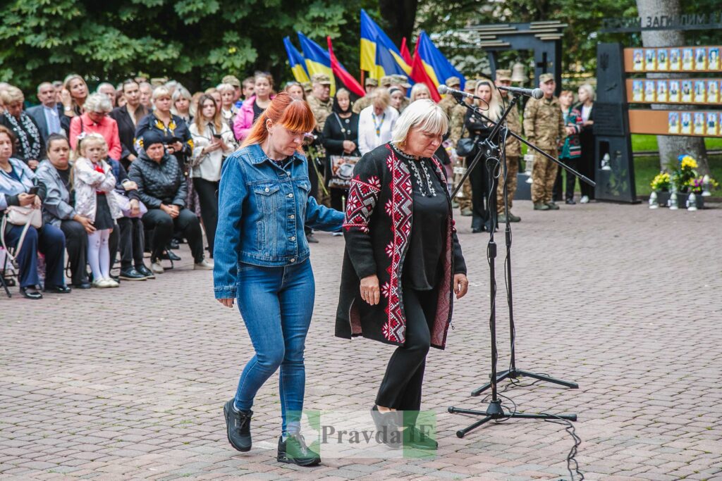 Урочистий захід з синьо-жовтими прапорами на задньому плані.