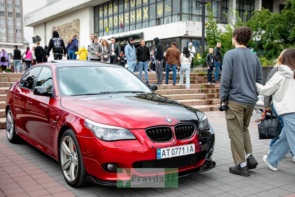 Червоний автомобіль BMW біля групи людей, вулиця.