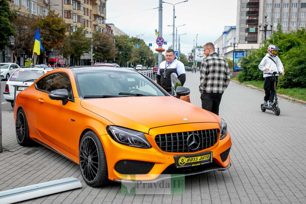 Помаранчевий автомобіль на вулиці біля людей