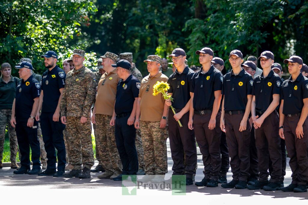 Люди в формі стоять на вулиці, тримають соняшники.