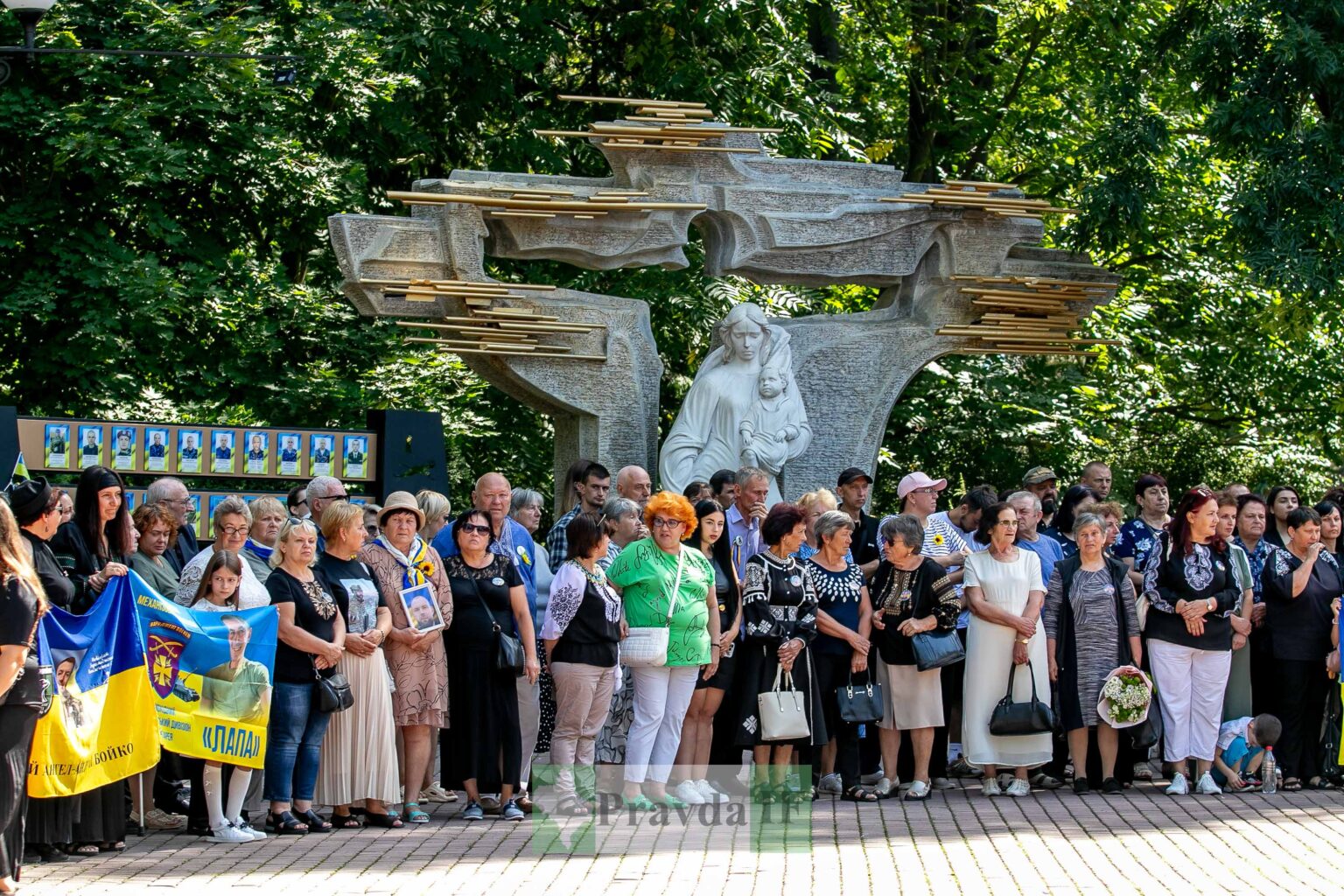 Люди перед пам'ятником на вулиці, на фоні дерева.