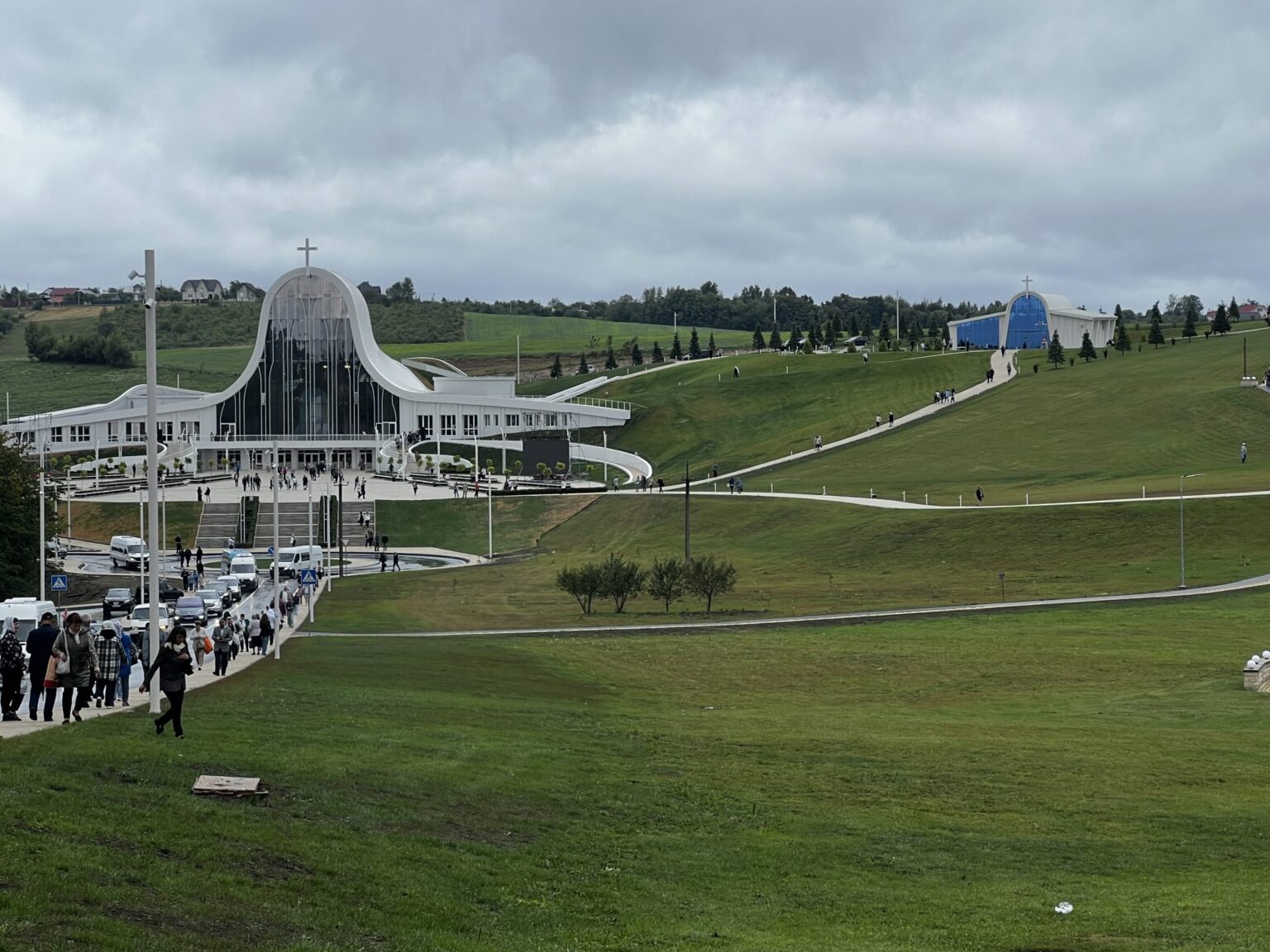 Сучасна церква на пагорбі з людьми і машинами.