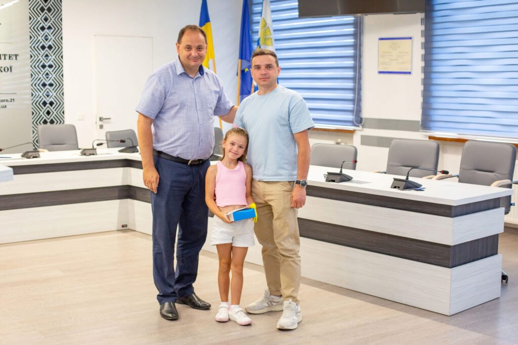 Люди стоять у приміщенні з прапорами.