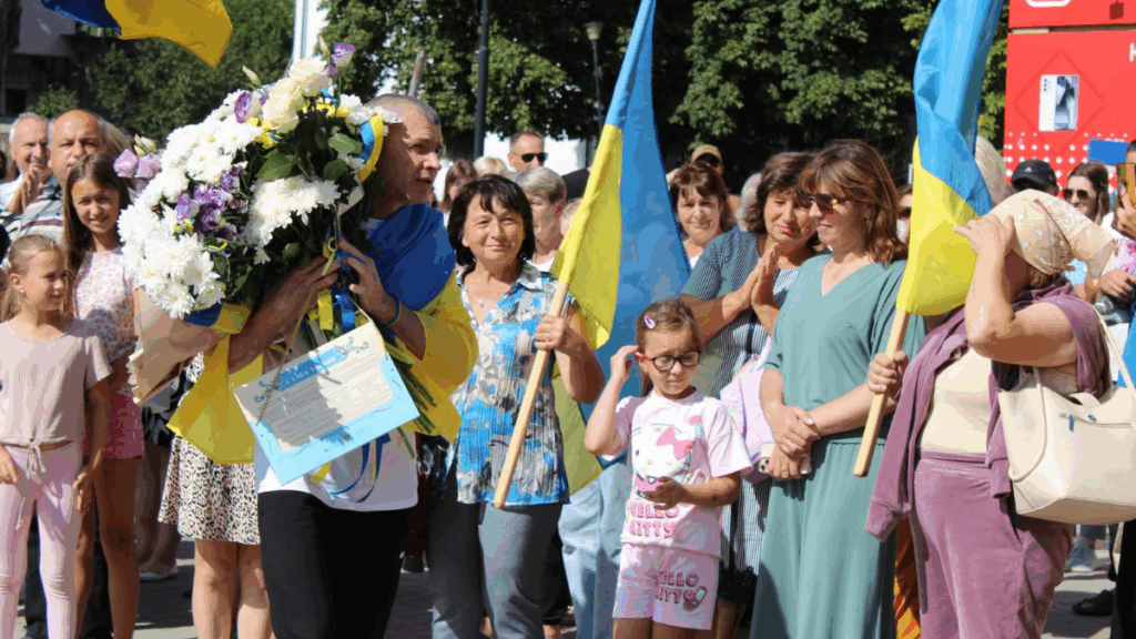 Люди з прапорами України й квітами на вулиці.