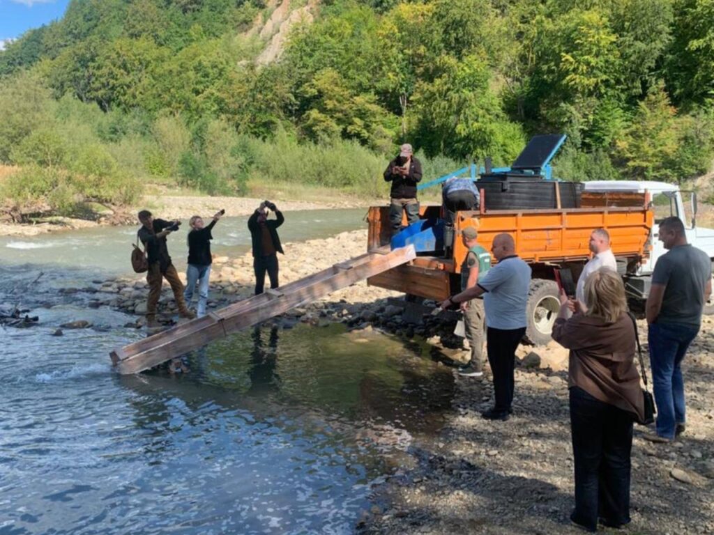 Група людей біля вантажівки, скидання риби в річку.