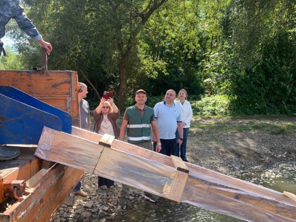 Люди біля ріки з дерев'яною конструкцією.