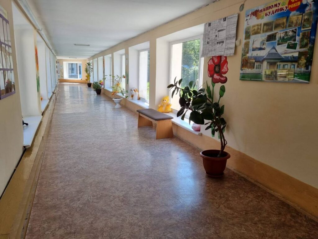 Довгий коридор з рослинами, вікнами та плакатами