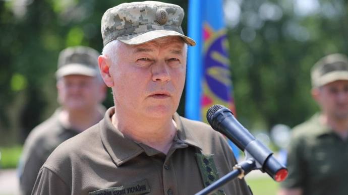 Військовий на мітингу з мікрофоном, прапор позаду.