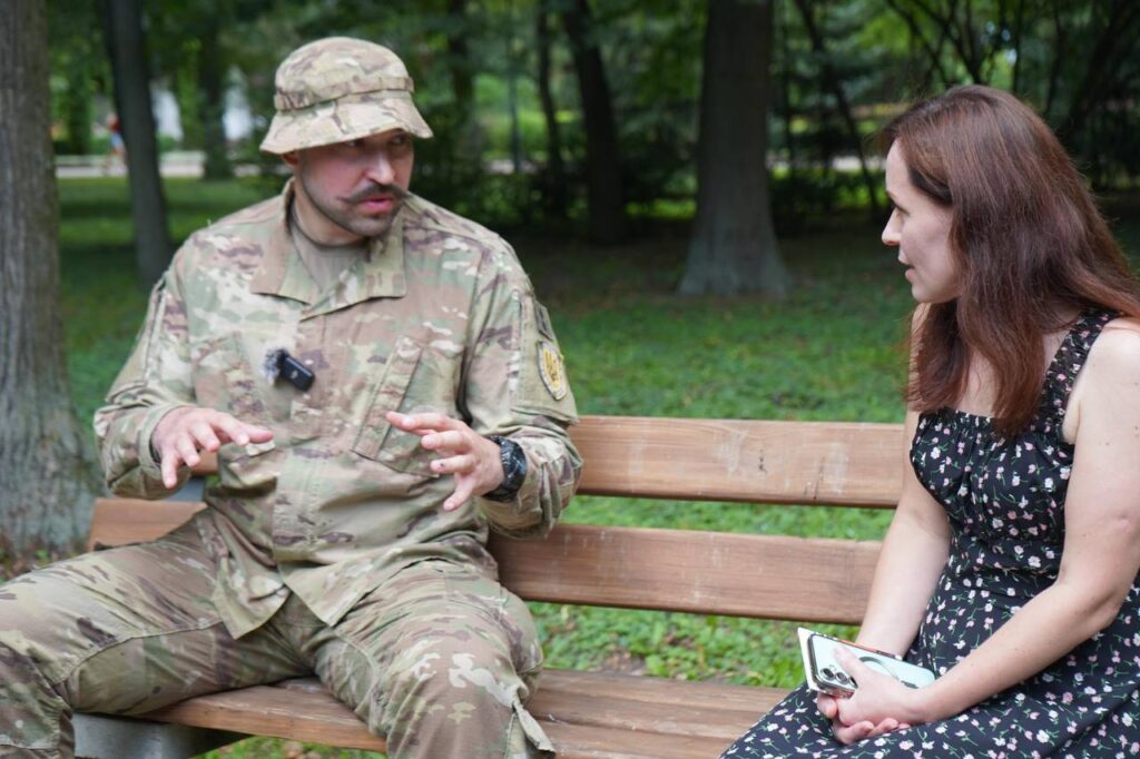 Солдат та жінка розмовляють на лавці в парку.