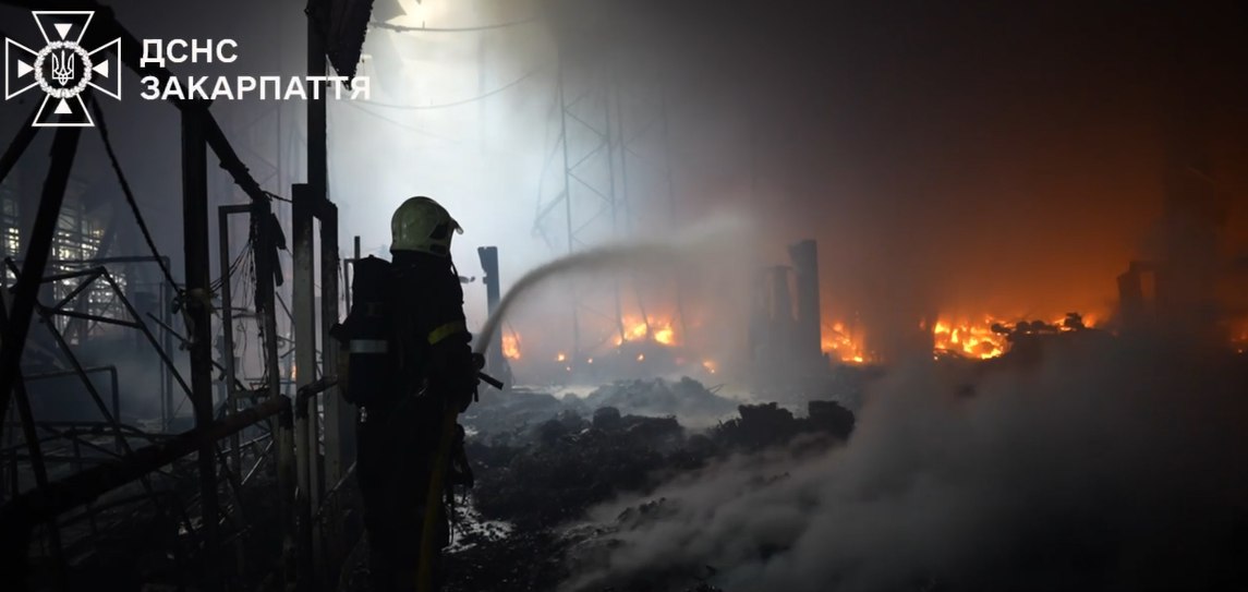 Пожежник гасить вогонь на заводі вночі.