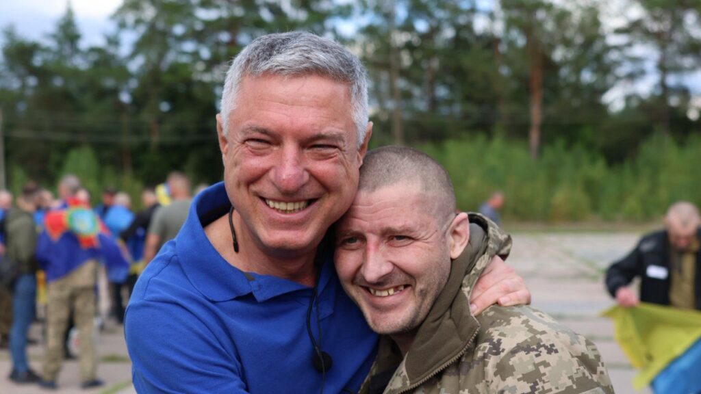 Двоє чоловіків обіймаються на вулиці з військовими