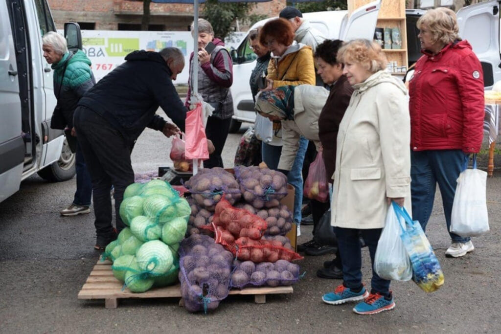 Люди на ринку купують овочі у продавця