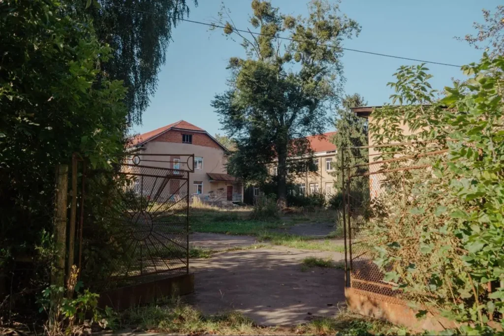 Занедбана будівля за металевими воротами на природі.