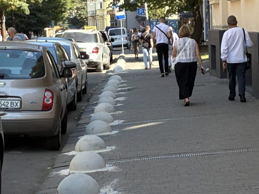 Люди йдуть тротуаром поряд з автомобілями