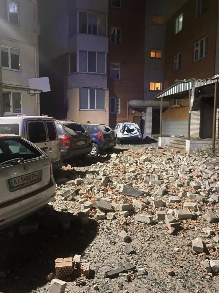 Завалені цеглою автомобілі біля багатоповерхівки вночі.