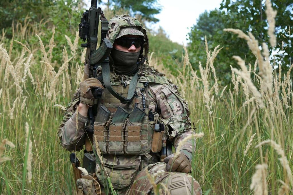 Військовий у камуфляжі сидить у траві лісу