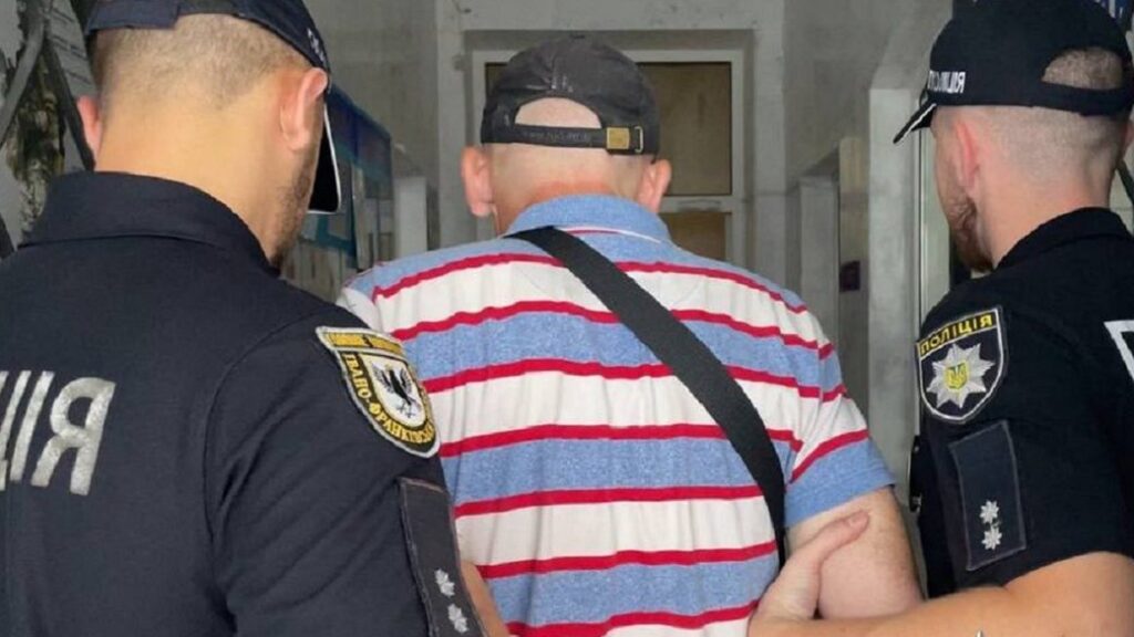 Чоловік у супроводі двох поліцейських у будівлі.