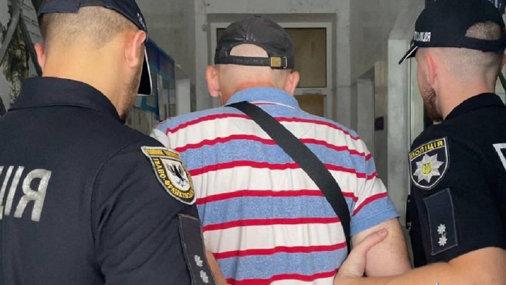 Чоловік у супроводі двох поліцейських у будівлі.